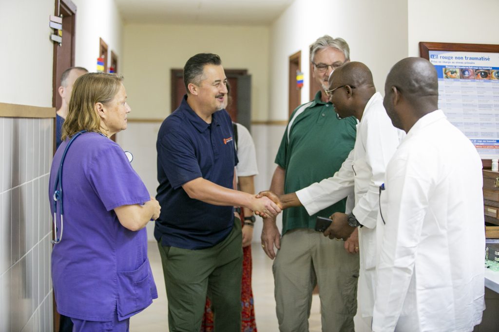 American man shakes hands with African doctor in white lab coat while others look on